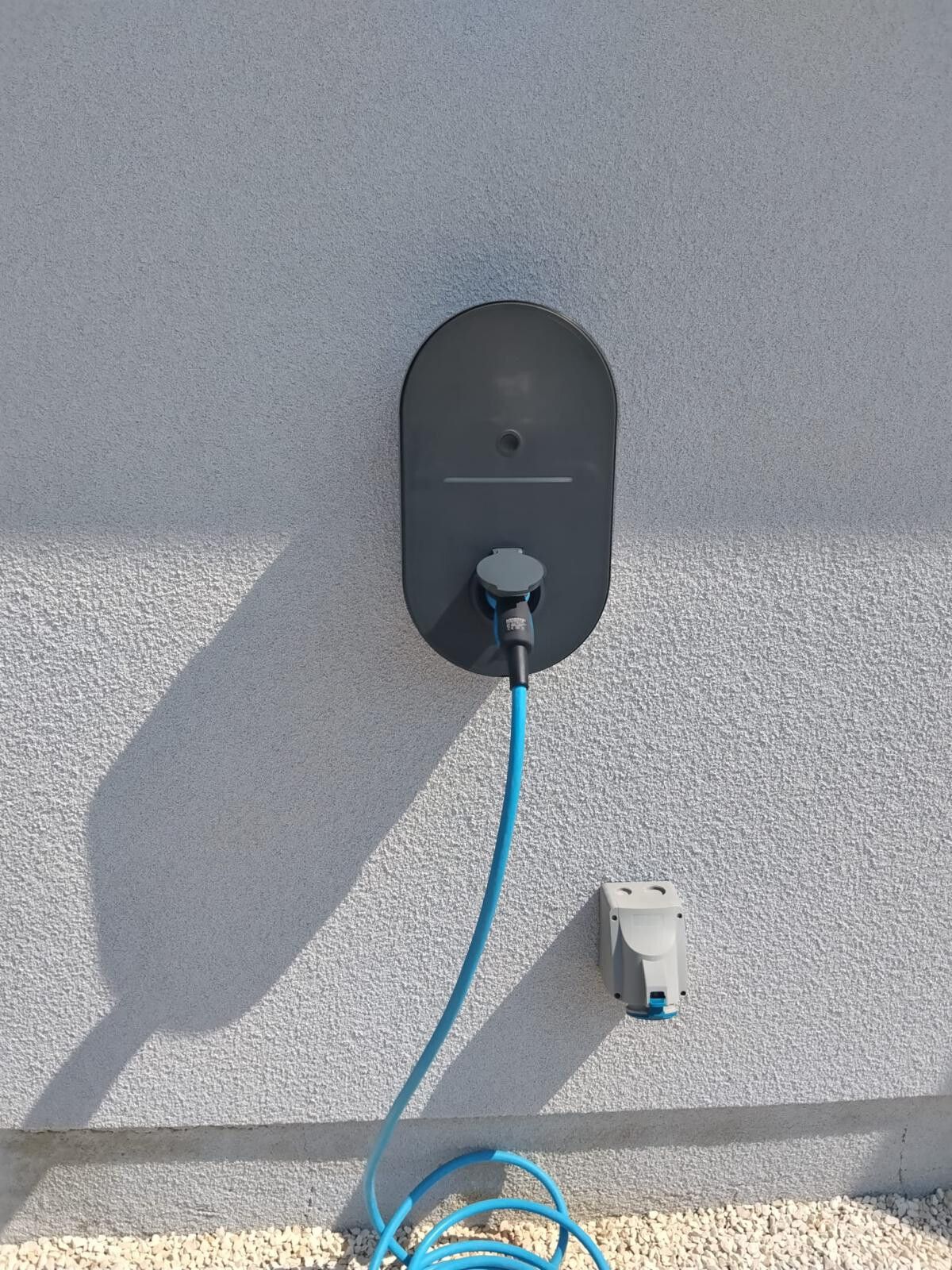 Borne de recharge murale avec son câble bleu branché, sur un crépi clair