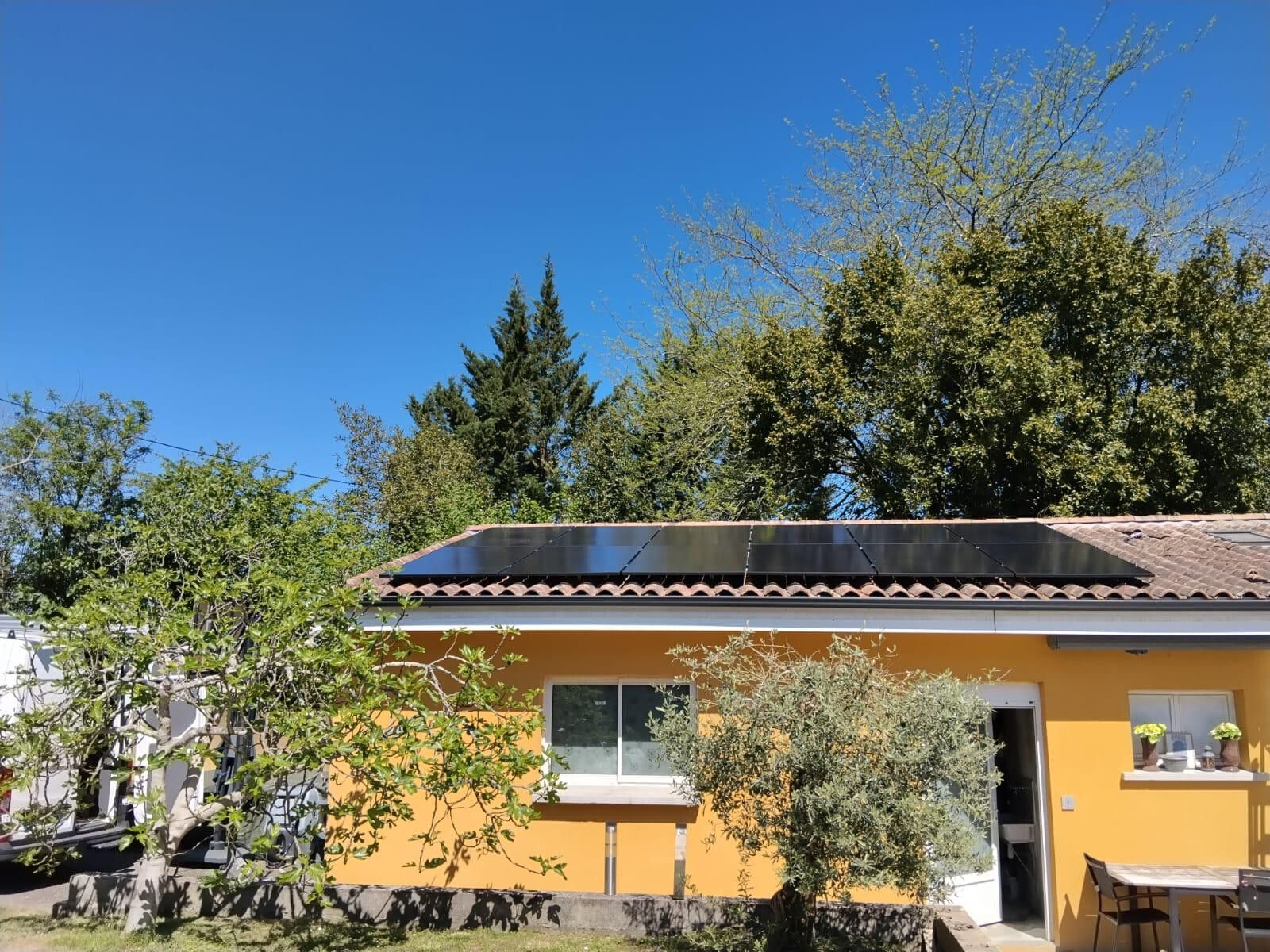 Maison jaune sous les arbres, rangée de modules photovoltaïques sur le toit