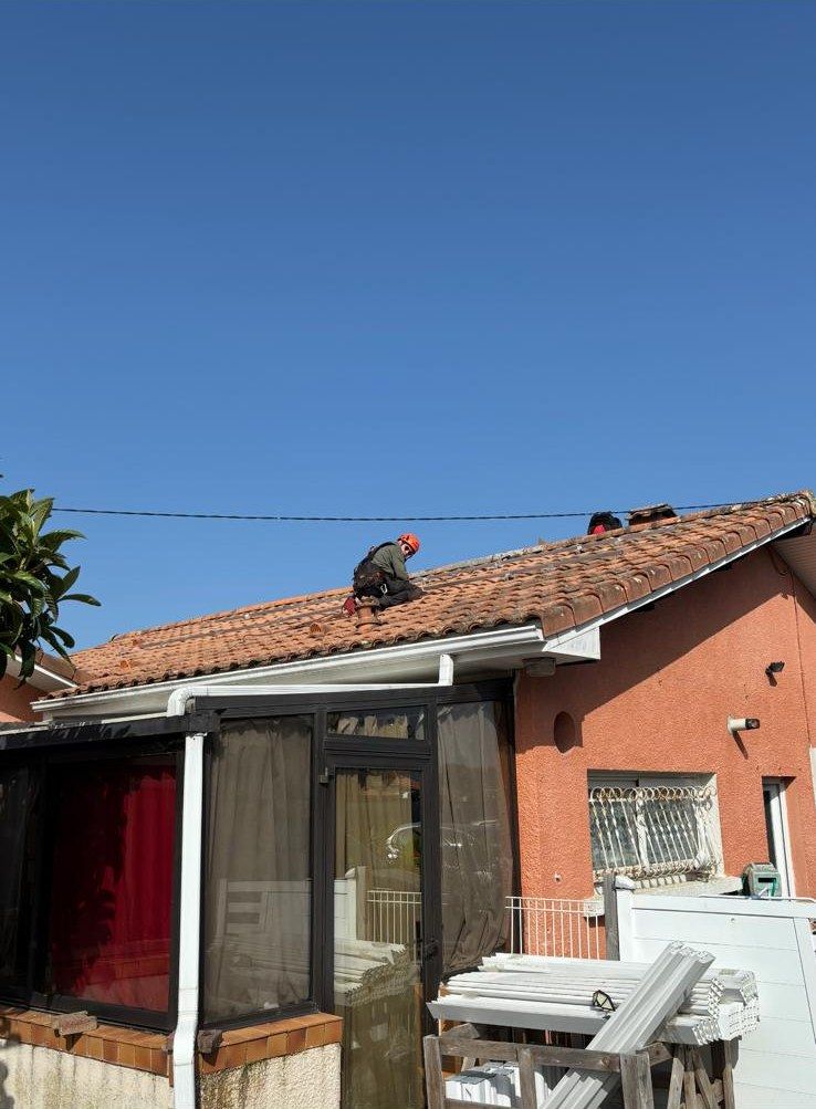 Un poseur casqué et harnaché sur un toit de tuiles, au-dessus d'une véranda