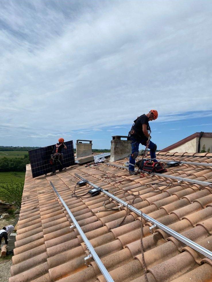 Deux poseurs encordés posent un module photovoltaïque sur ses rails, vignes en arrière-plan