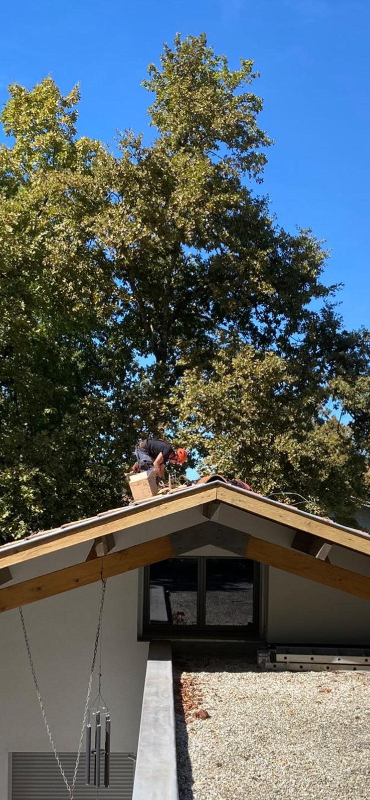 Un poseur casqué au faîtage d'un toit, sous un grand arbre