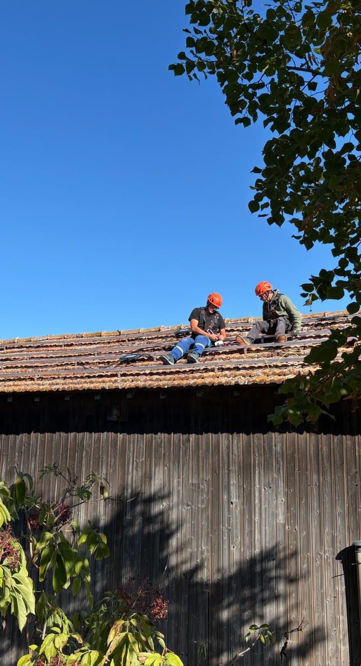 Deux poseurs casqués assis sur les rails d'un toit de grange en bardage bois