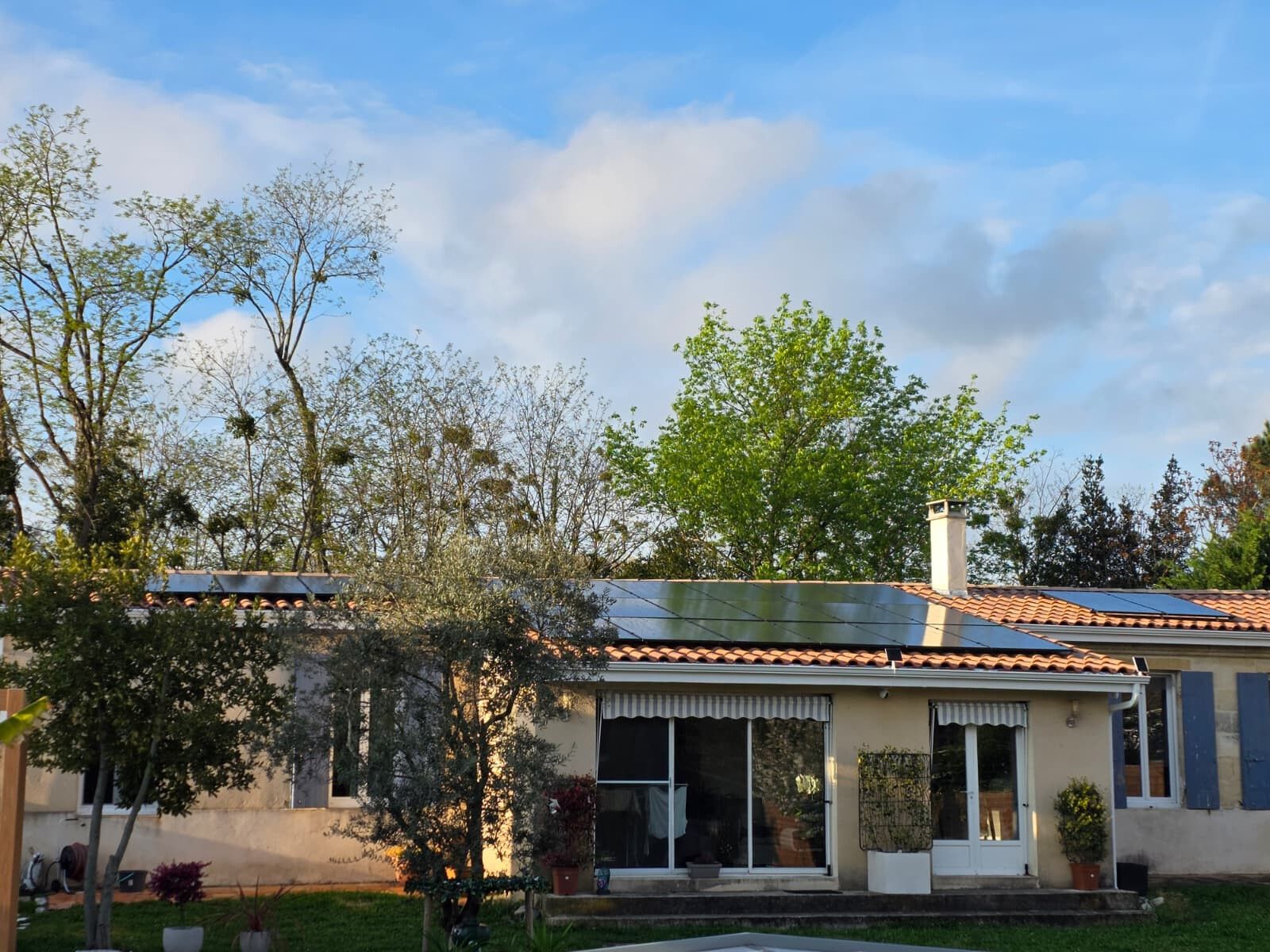 Maison girondine en fin de journée, vue du jardin, avec ses modules photovoltaïques sur le toit de tuiles canal