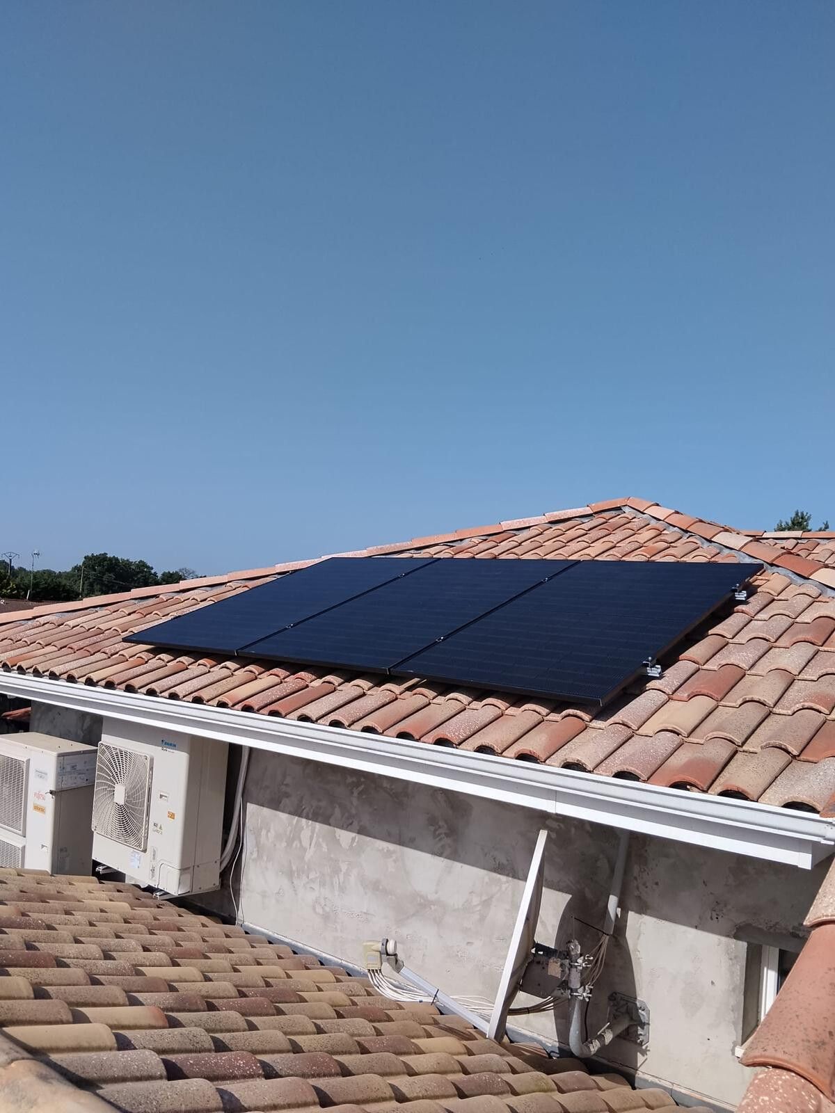 Deux unités extérieures de pompe à chaleur posées sur une façade, trois modules photovoltaïques sur le toit au-dessus